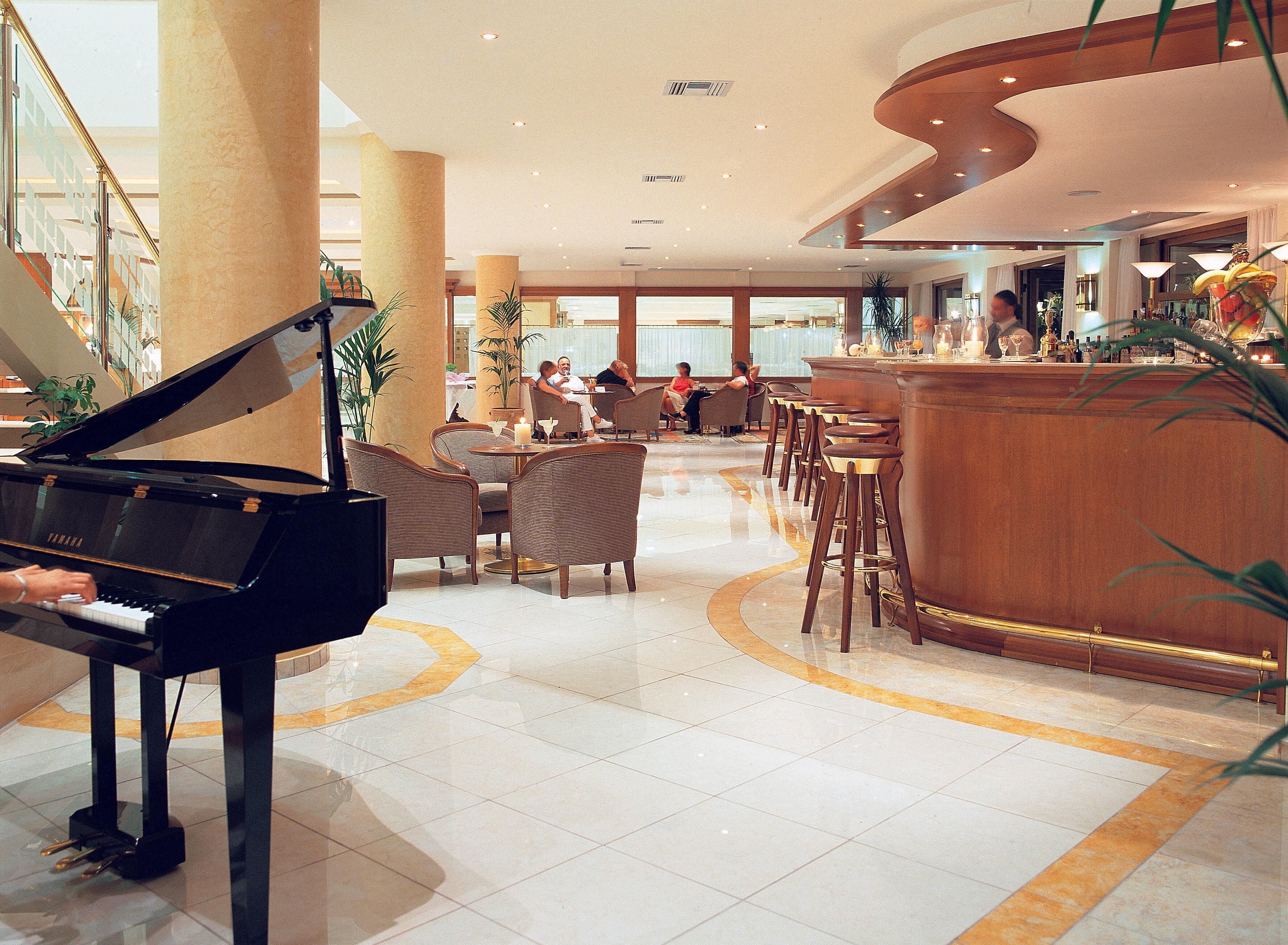 A grand piano in a spacious lobby with a bar area and seating.