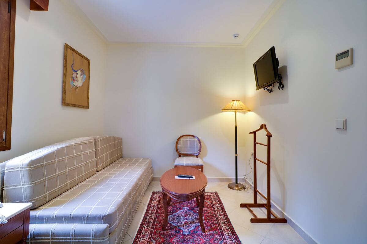 Une pièce comprenant un canapé, une petite table, une chaise, un lampadaire et un téléviseur fixé au mur.