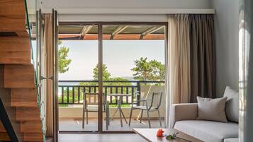 A modern living room with a sofa, a coffee table, and a balcony with a view of greenery and a body of water.