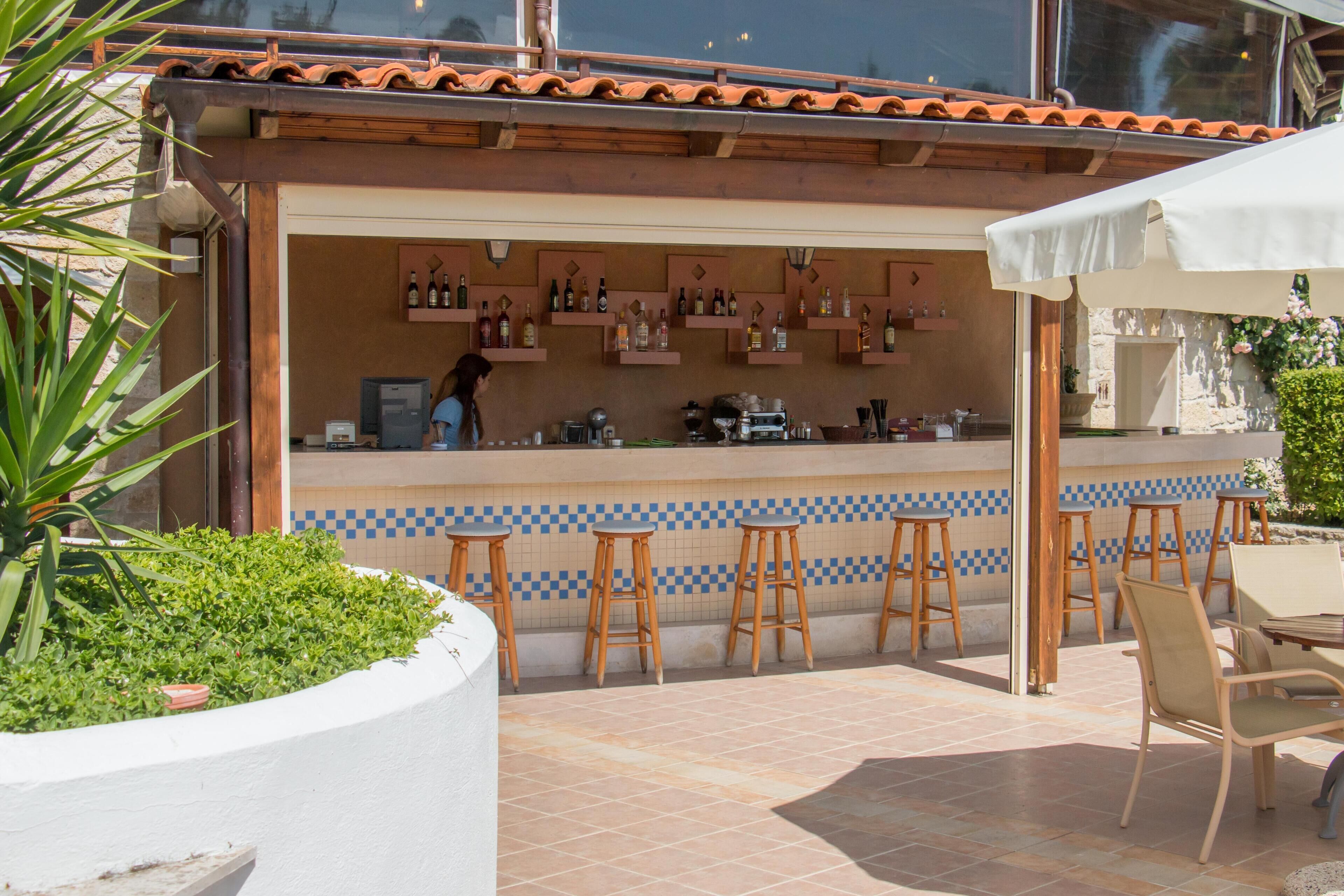 An outdoor bar area with stools, a counter with bottles, and a chef preparing food.