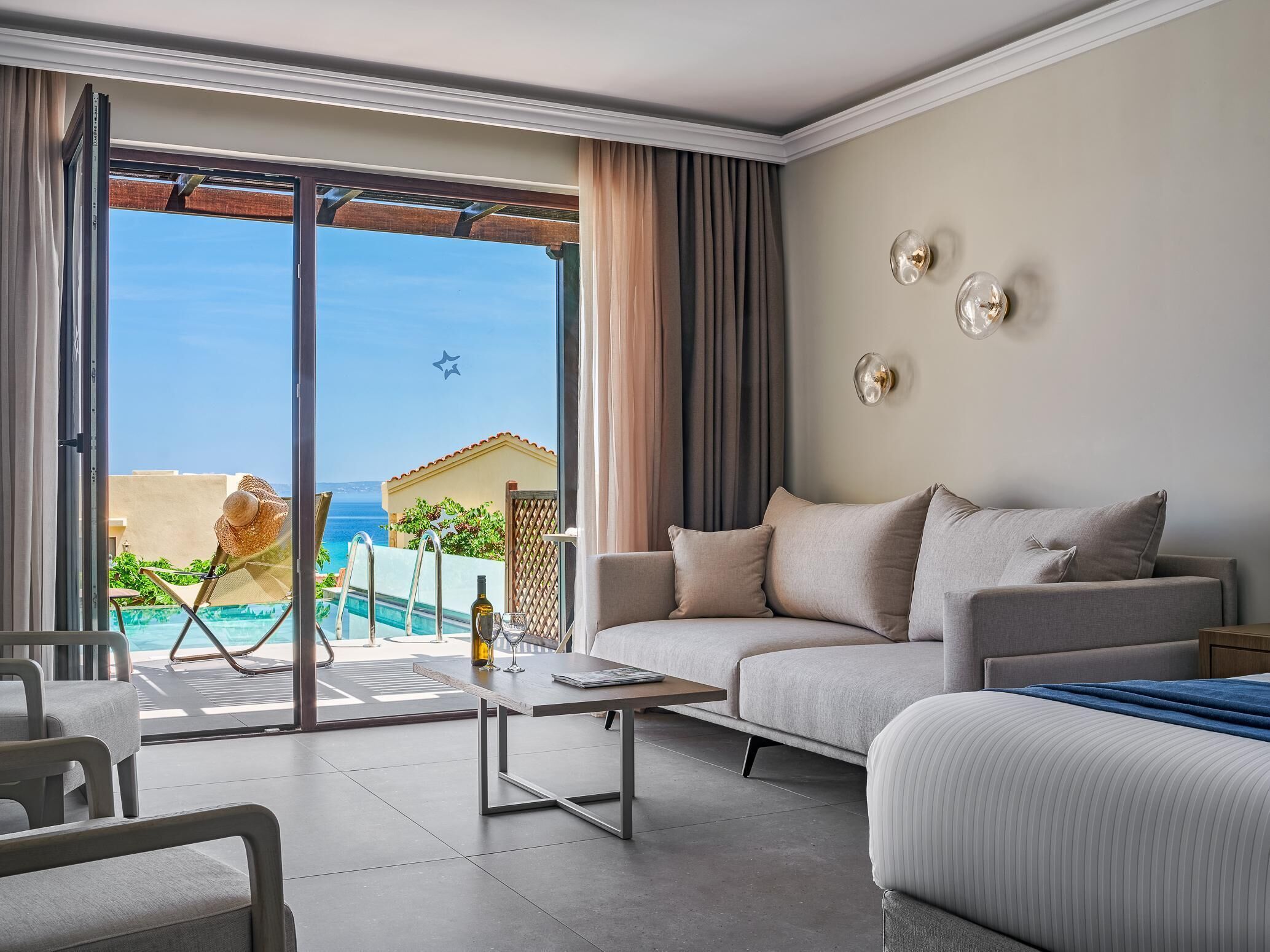 A modern living room with a sofa, a coffee table, and a view of a pool and ocean.