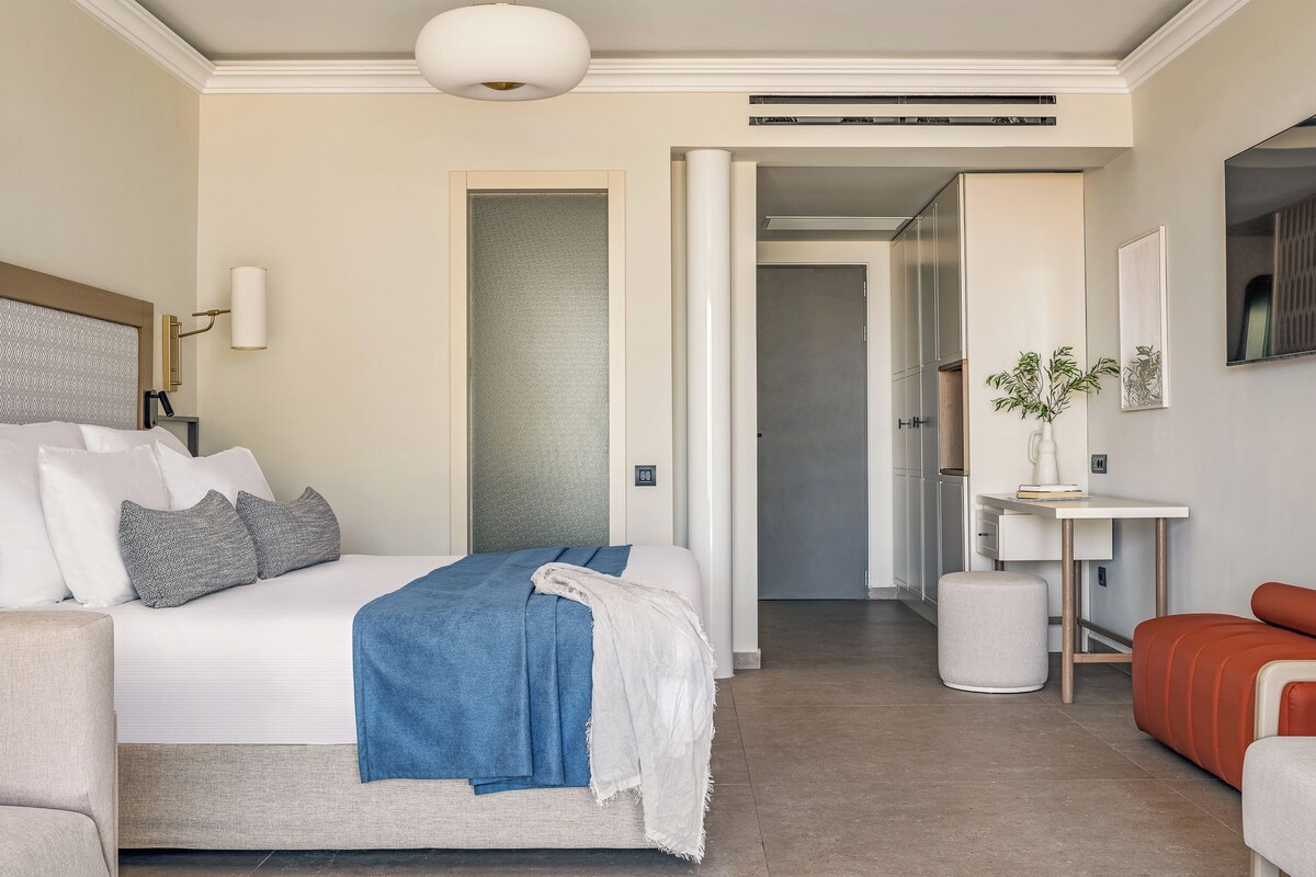 A modern hotel room with a large bed, a desk, and a seating area.