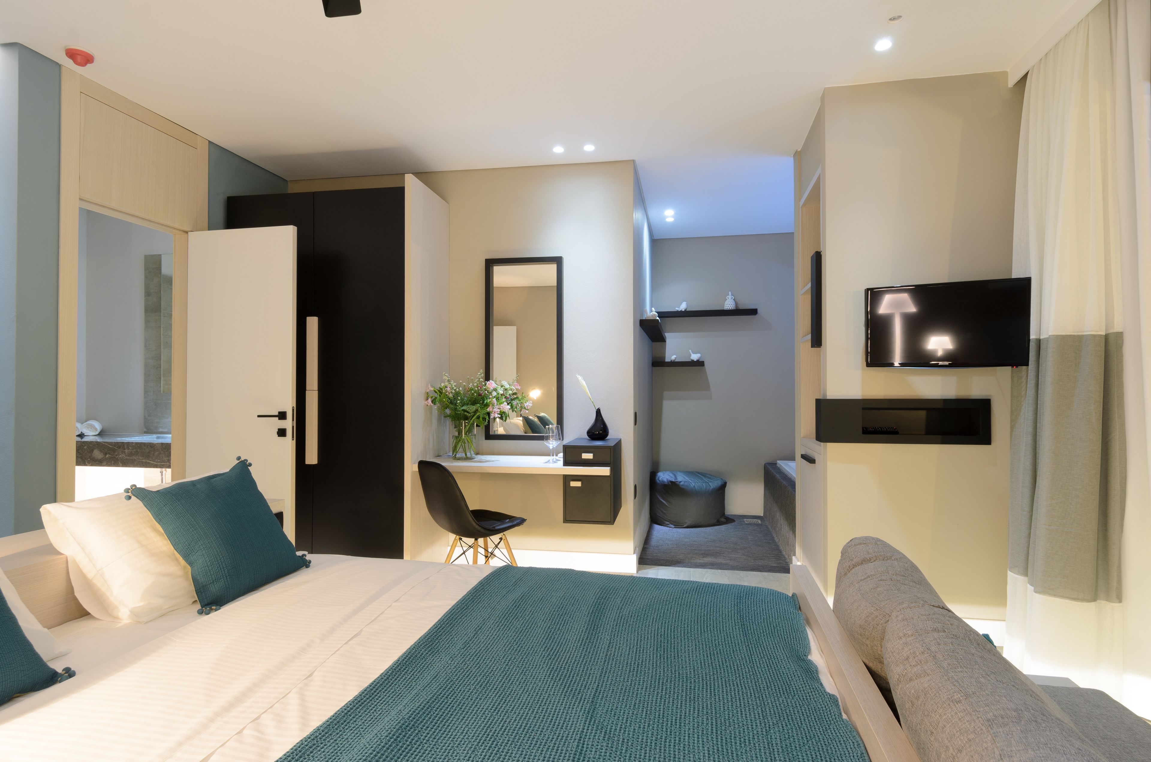 A modern hotel room with a bed, a desk, a chair, a TV, and a bathroom visible through an open door.