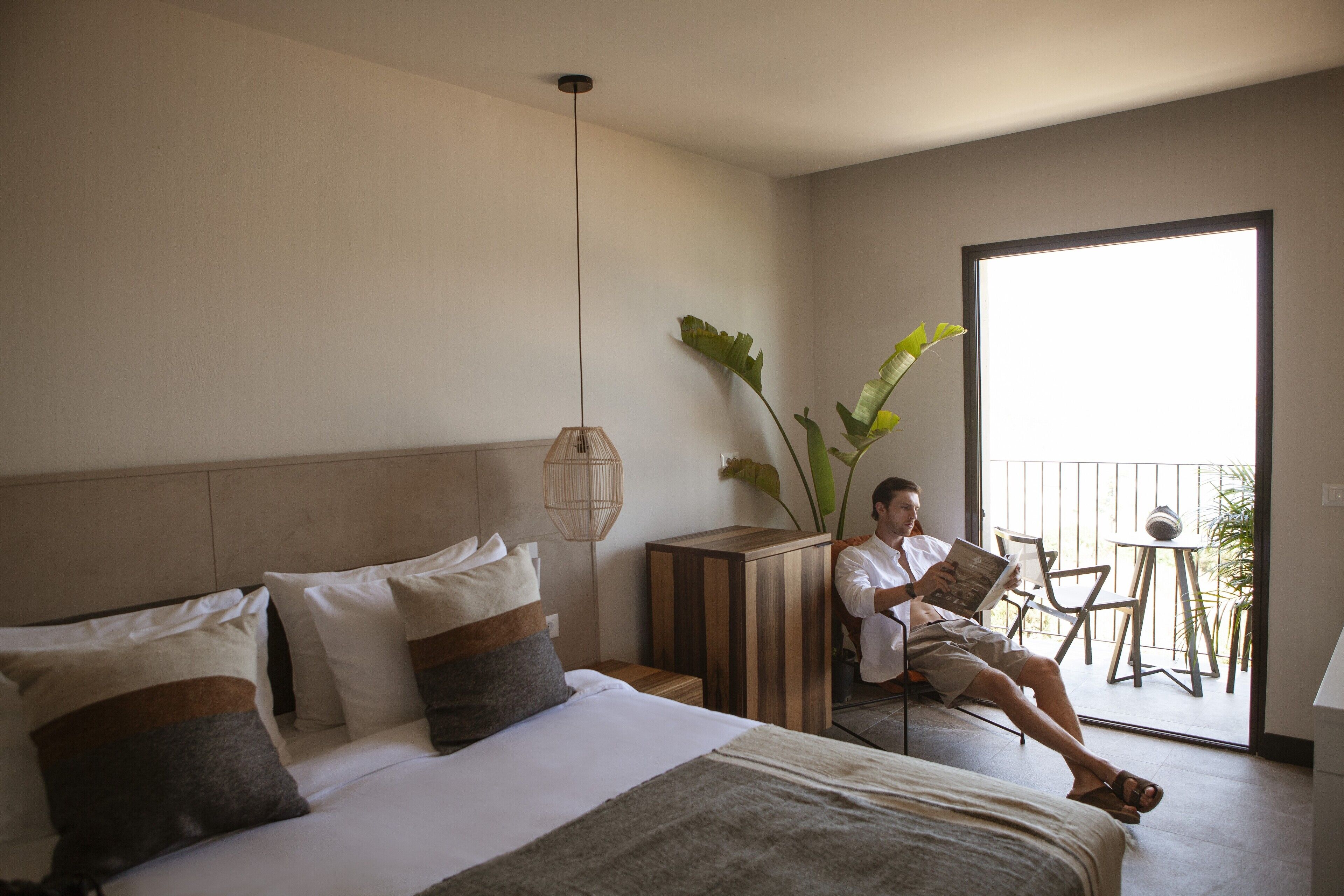 A hotel room with a bed, bedside table, reading lamp, and a view of the outside balcony.