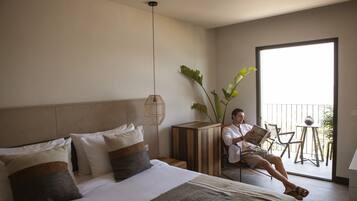 A hotel room with a bed, bedside table, reading lamp, and a view of the outside balcony.
