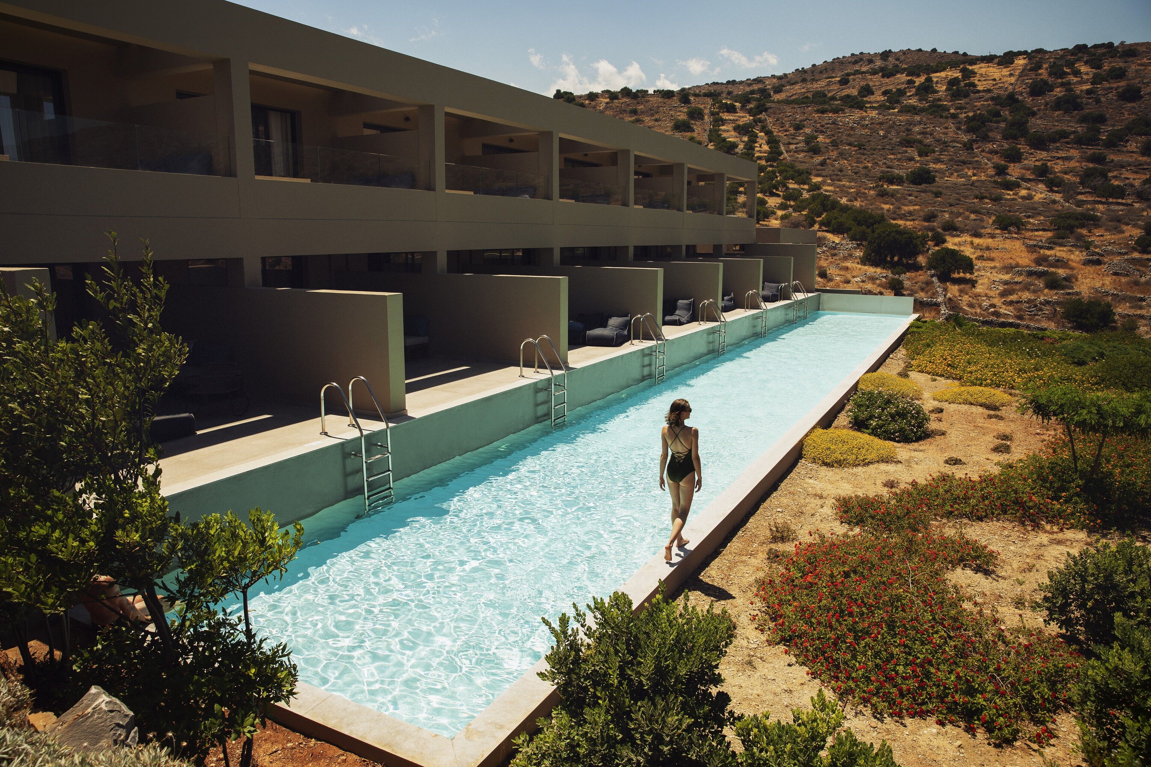 Una piscina adiacente a un edificio moderno con numerosi balconi, circondata da verde curato e un paesaggio collinare.