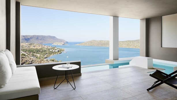 Una habitación moderna con un ventanal grande, piscina, sofá y una mesita.