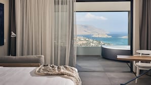 Un dormitorio con cama, una silla, una mesa y vistas a un paisaje costero.