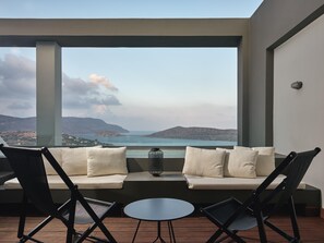 A balcony with a sofa, chairs, and a small table, overlooking a scenic view of hills and a body of water. - Domes Aulus Elounda, All-Inclusive Resort, Curio Collection by Hilton - Adults Only (Agios Nikolaos)