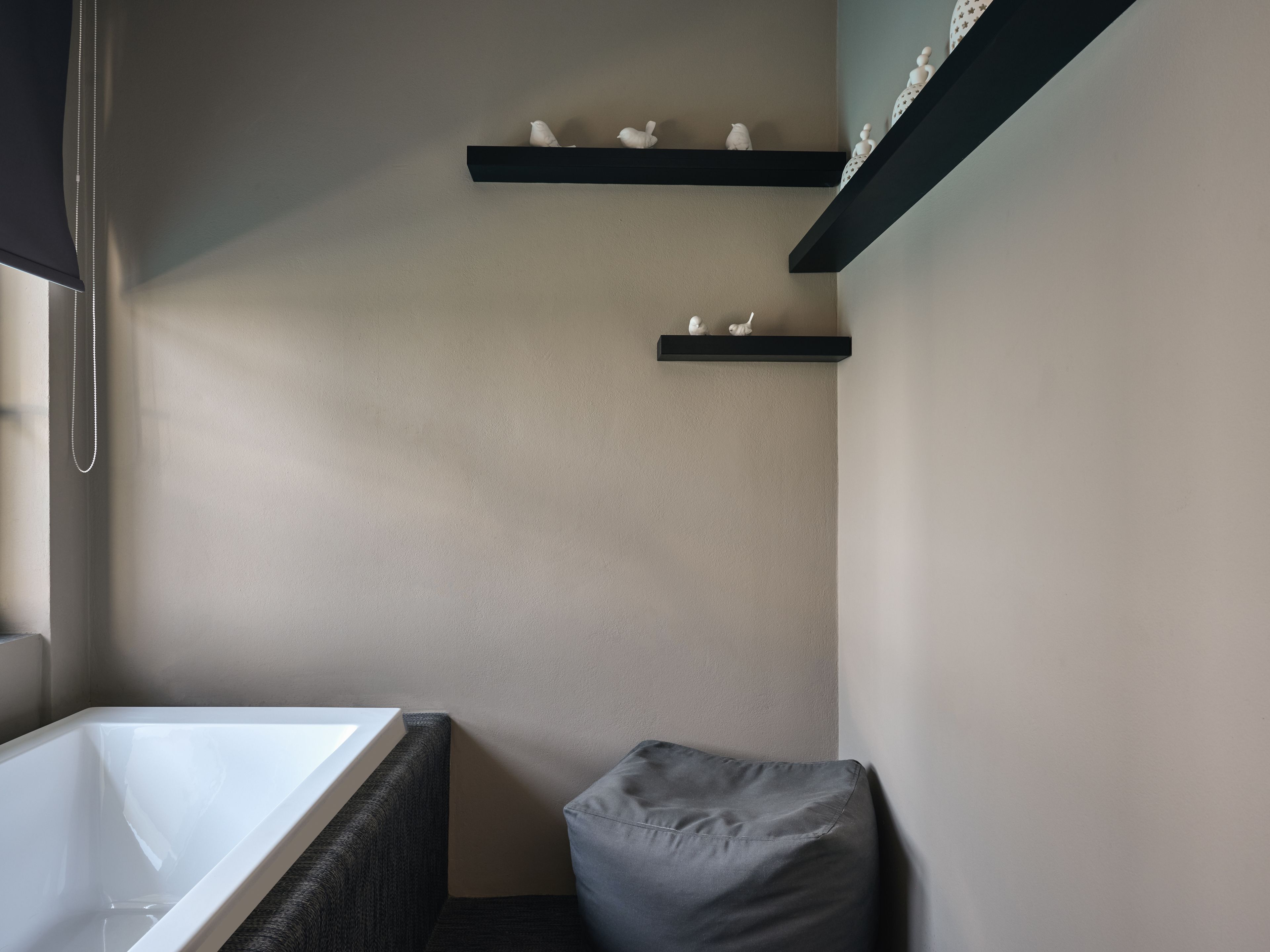 A modern bathroom with a bathtub, dark-colored walls, and two black shelves with decorative items.