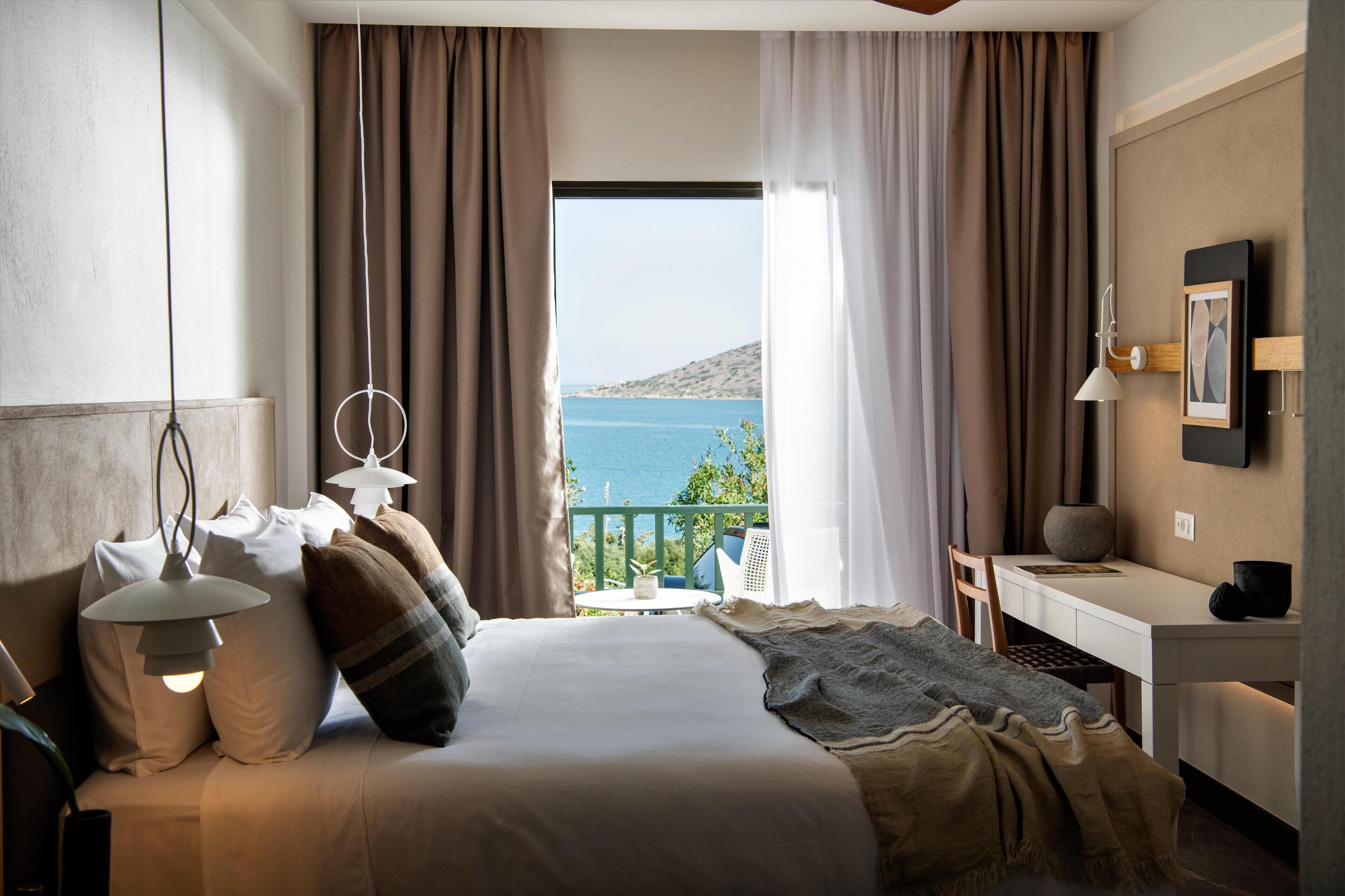 Un dormitorio con cama, lámparas de noche, un escritorio y vista al mar.