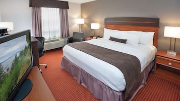 A hotel room with a large bed, a desk with a computer, a TV, and a window with curtains.