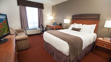 A hotel room with a large bed, a desk, a chair, a desk lamp, a bedside table, and a wall-mounted TV.