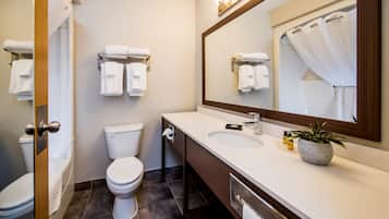 Un baño moderno con inodoro, lavabo y espejo. Hay toallas colgadas en la pared y una planta en maceta sobre el mostrador.