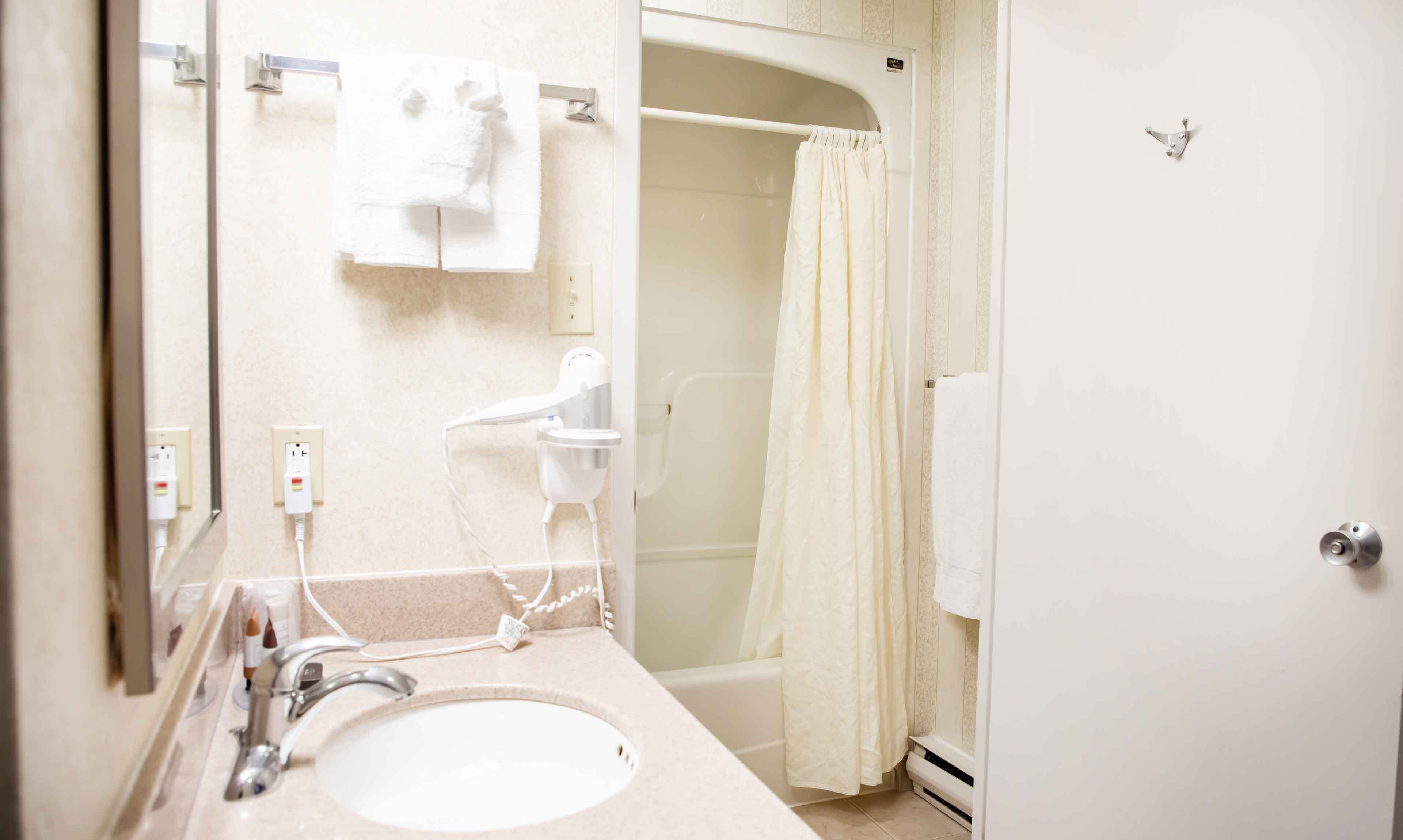Un baño con lavamanos, espejo, toallero, cortina de ducha y una puerta.