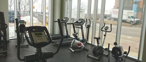 A gym with stationary bikes and treadmills, large windows, and a view of the street outside.