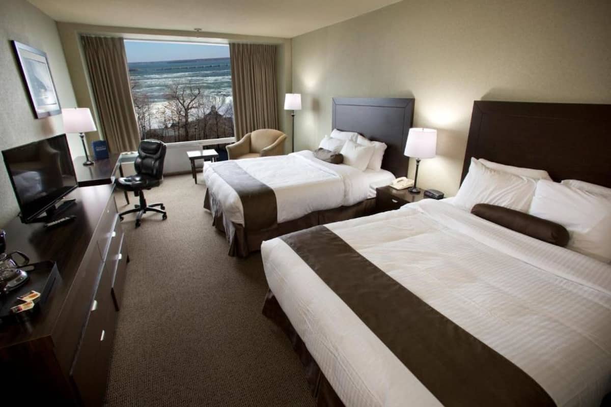 Habitación de hotel con dos camas, un escritorio con computadora, televisión y vista al océano.