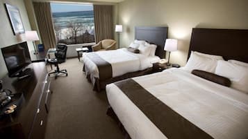 Quarto de hotel com duas camas, uma mesa com computador, televisão e vista para o oceano.
