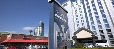 A hotel sign with a view of a city skyline, a parking lot, and a building with a red awning.