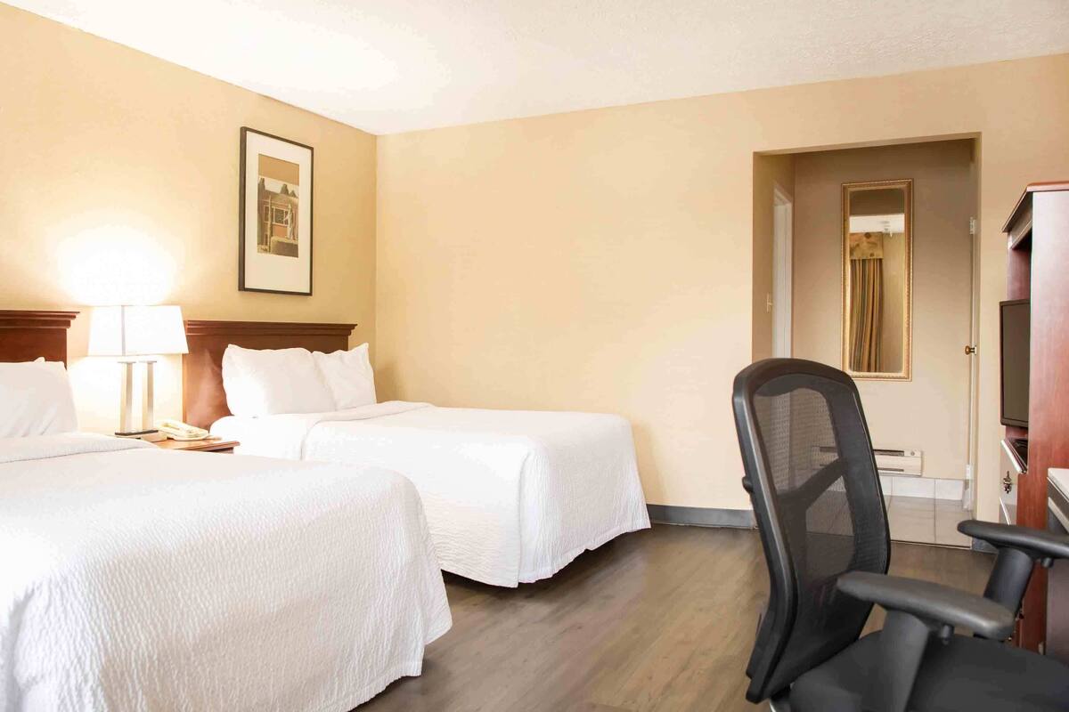 Una habitación de hotel con dos camas, un escritorio, una silla y un televisor.