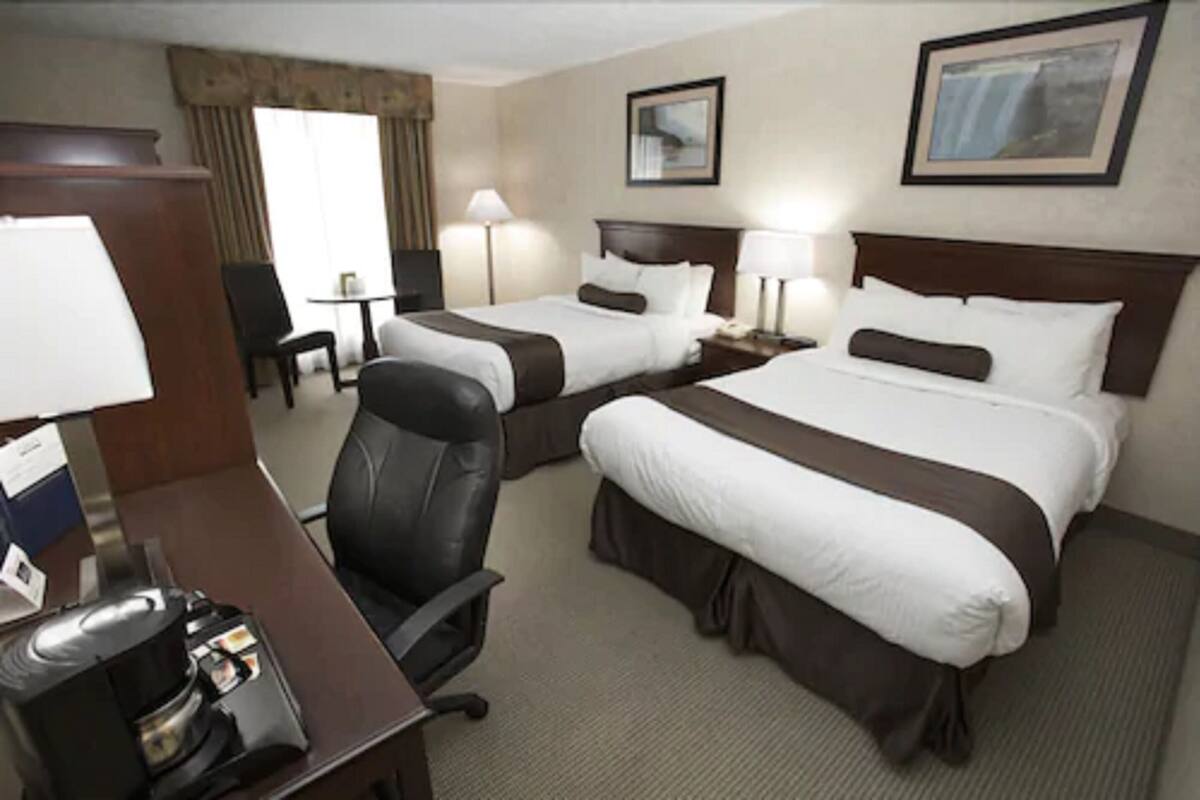 Habitación de hotel con dos camas, un escritorio con cafetera, una silla y una lámpara.