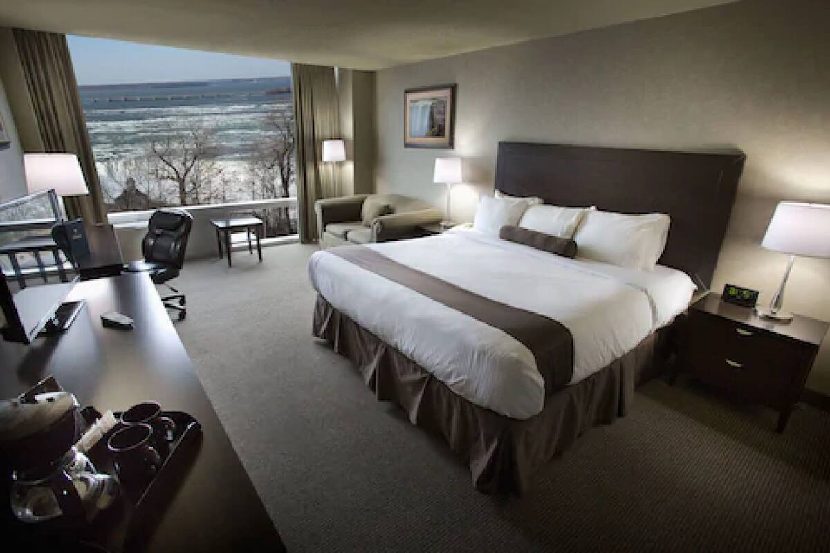 Habitación de hotel con una cama grande, un escritorio con computadora, una silla y vistas al exterior.