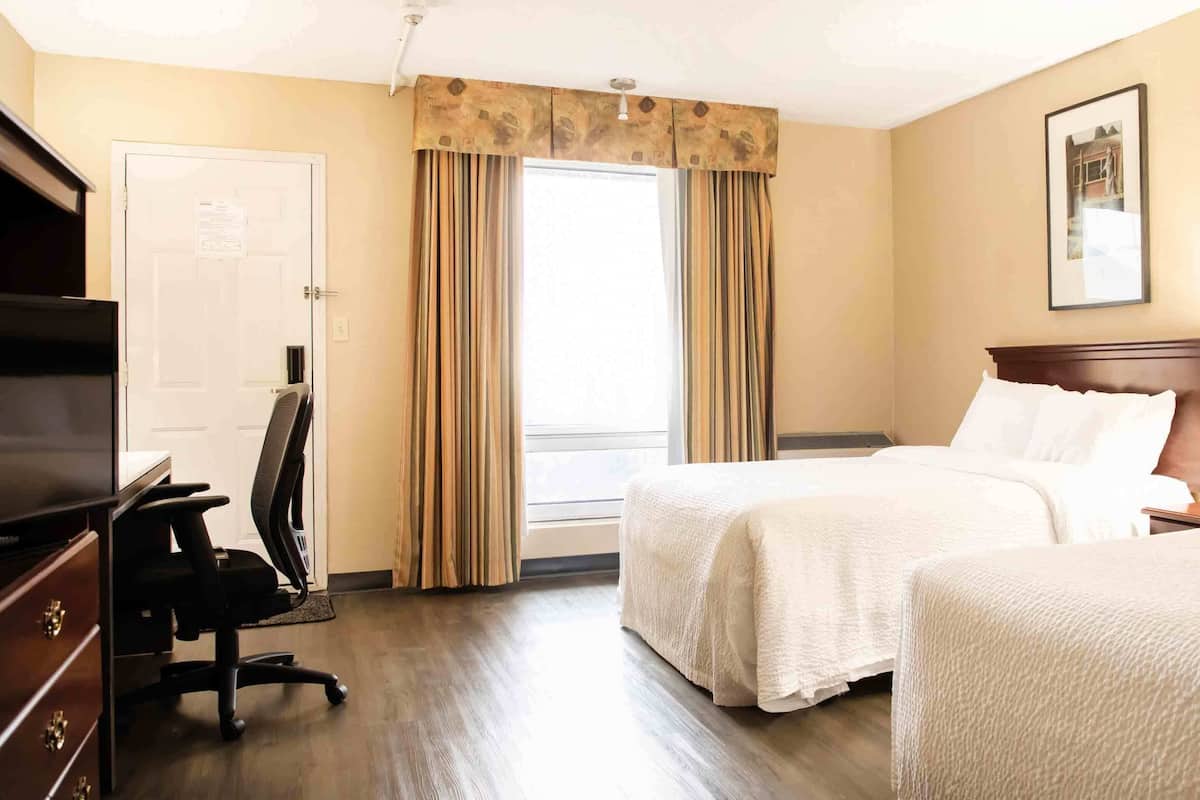 Una habitación de hotel con dos camas, un escritorio con silla, televisión y ventana con cortinas.
