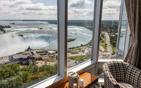 A room with a large window overlooking a waterfall and a distant cityscape.
