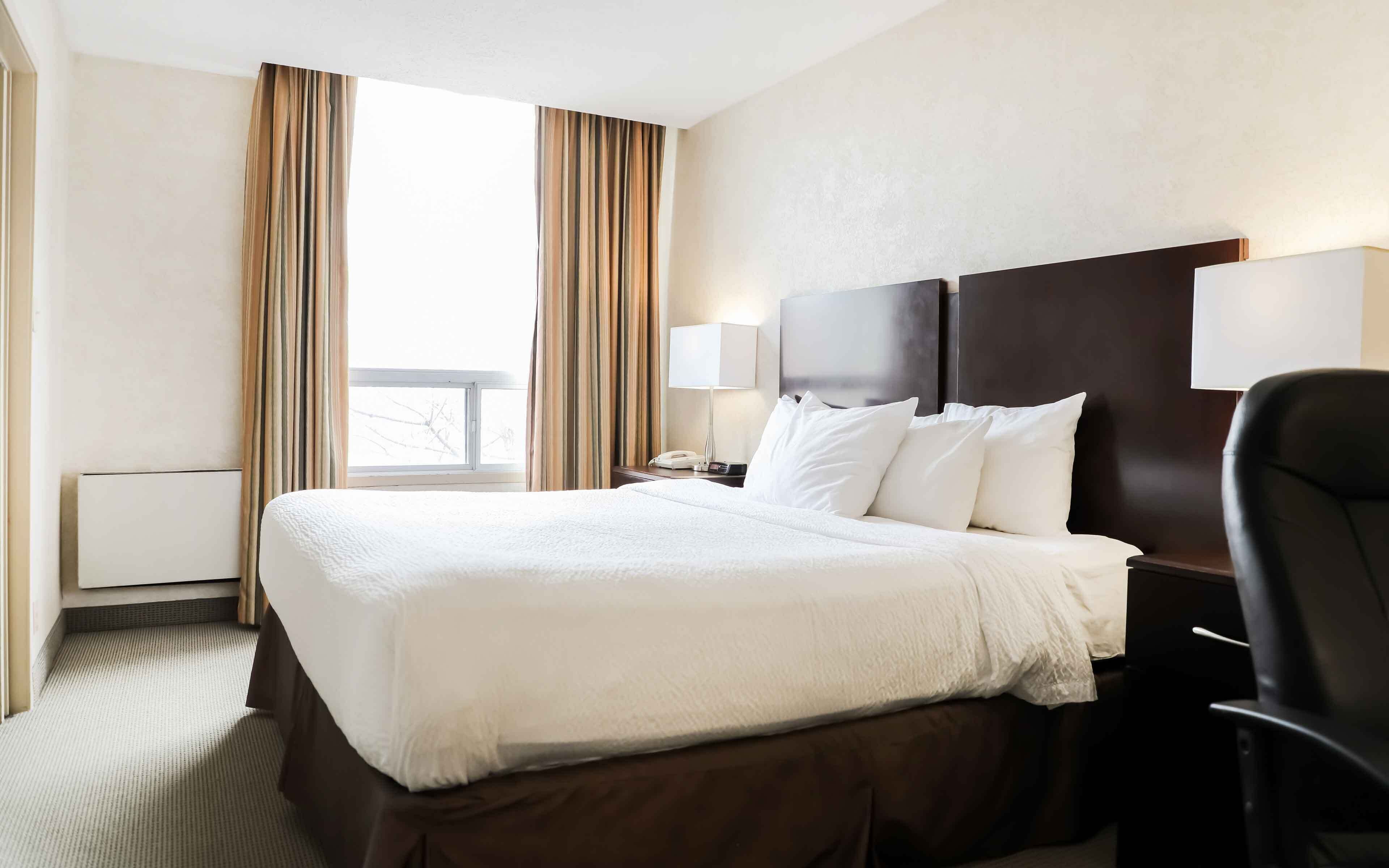 Une chambre d’hôtel avec un grand lit, un bureau, une chaise, une lampe et une vue sur l’extérieur.