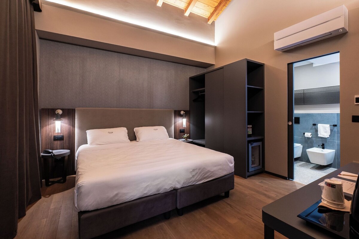 Habitación de hotel moderna con una cama grande, mesitas de noche, un equipo de aire acondicionado y vistas al baño.