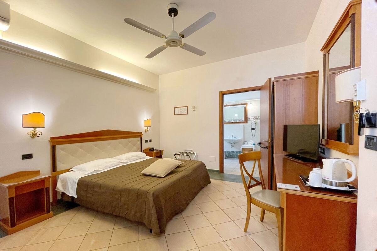 A hotel room with a bed, a desk, a chair, a television, and a bathroom visible through an open door.