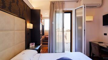 Habitación de hotel con una cama grande, un escritorio, una silla, un televisor y un balcón con vistas.