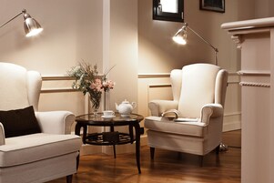 Una habitación con dos sillones, una mesita redonda con tetera y taza, y un jarrón con flores.