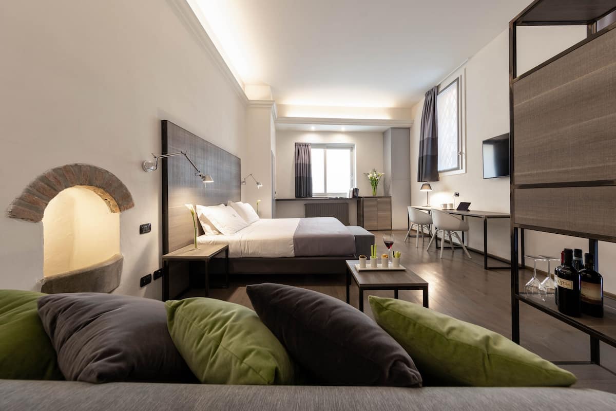 A modern hotel room with a bed, a sofa, a desk, and a TV.