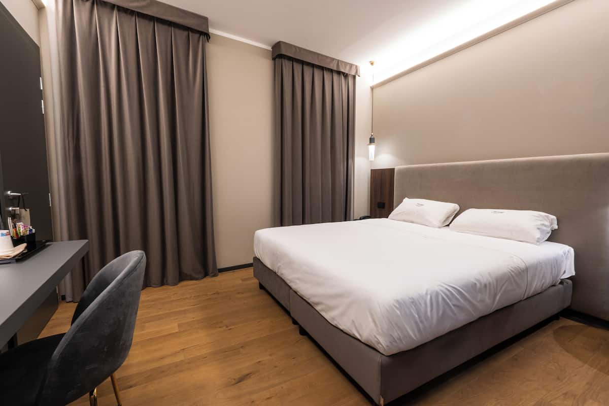 A modern hotel room with a large bed, a desk, and a chair.