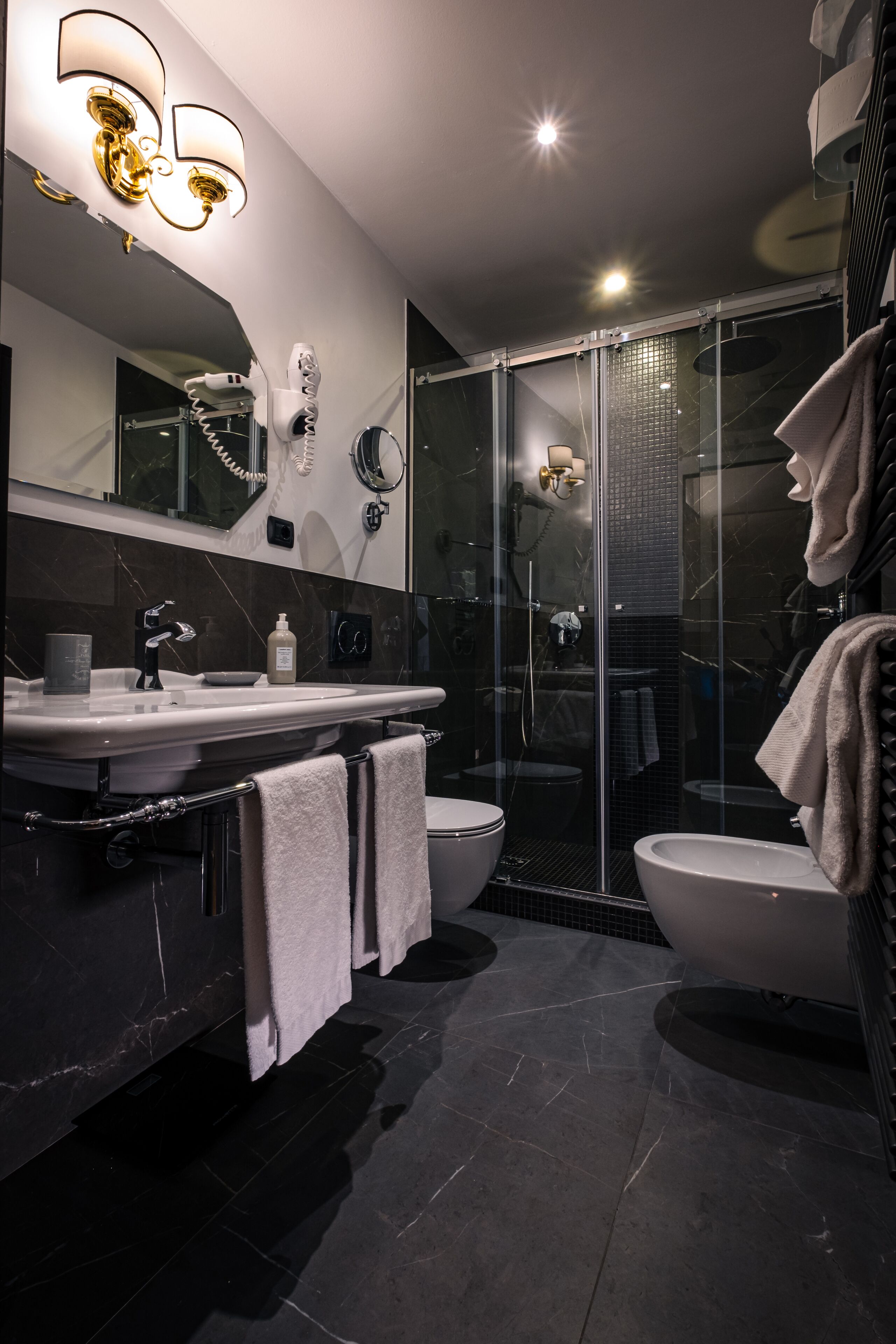 Une salle de bain moderne avec une douche à parois de verre, deux toilettes, un meuble-lavabo avec un miroir et un porte-serviettes.