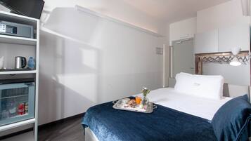 Una habitación de hotel con una cama, una bandeja con productos de desayuno, un minibar y un armario.