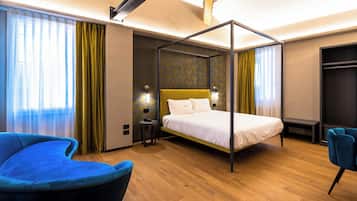 A modern hotel room with a four-poster bed, a blue armchair, a bedside table, and a wardrobe.