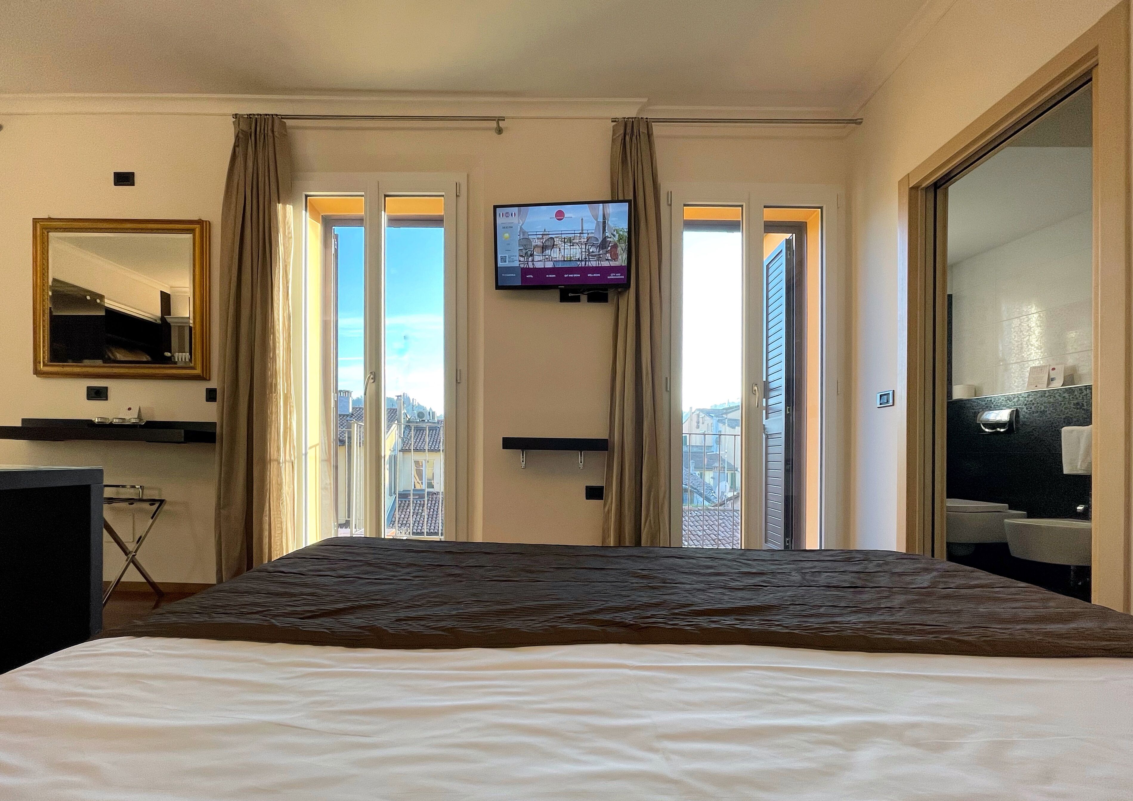 Une chambre d’hôtel avec un lit, une télévision, un balcon avec des rideaux et une vue sur le paysage urbain.