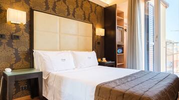Habitación de hotel con una cama grande, una mesita de noche, una lámpara y vistas de la ciudad a través de la ventana.