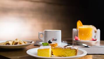 A table with a plate of yellow cake, a white mug, and a glass of orange juice.