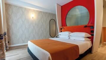 A modern hotel room with a large bed, a red accent wall, and a round mirror.