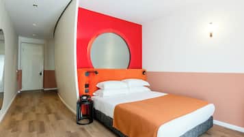 Una camera d'albergo con un letto, uno specchio rotondo a parete, un telefono e un comodino.