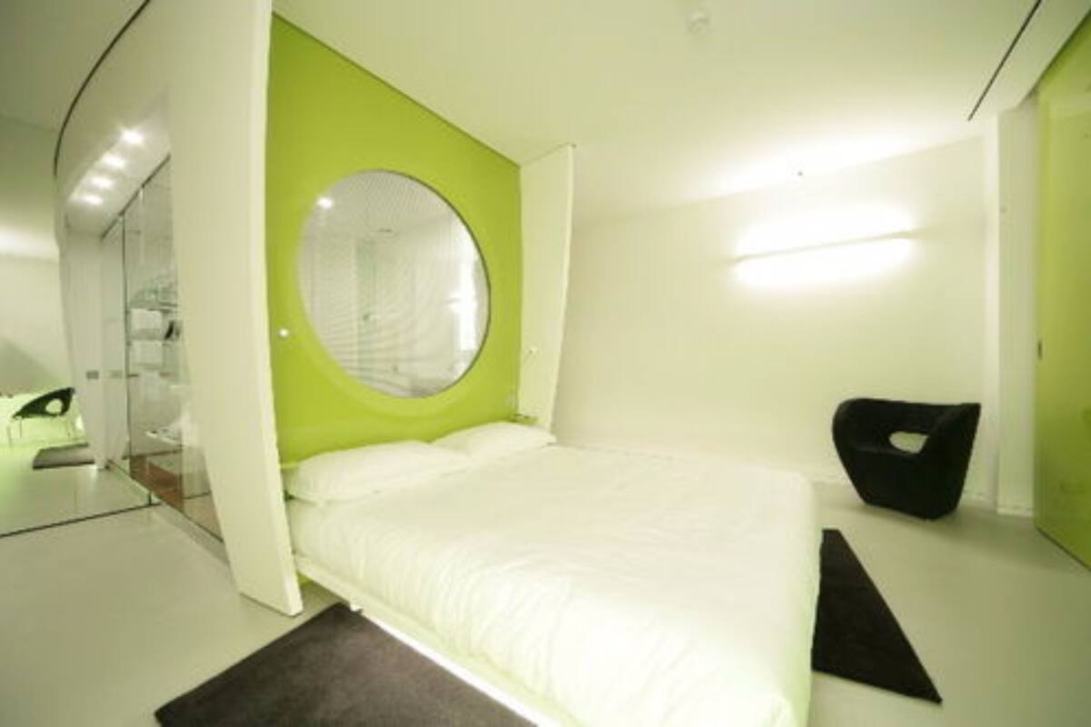 A modern bedroom with a bed, a round mirror, and a black chair.