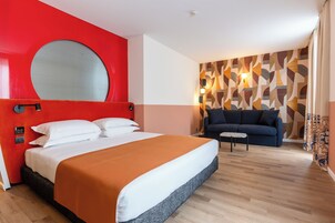 Habitación de hotel con una cama grande, una pared de acento roja, un diseño de pared estampado, un sofá azul y una mesita pequeña.