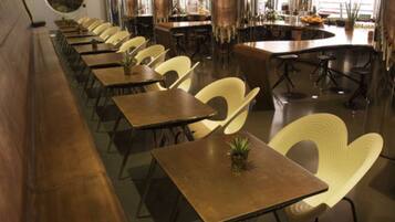 A long dining area with multiple tables and chairs, a bar area with stools, and large windows allowing natural light.