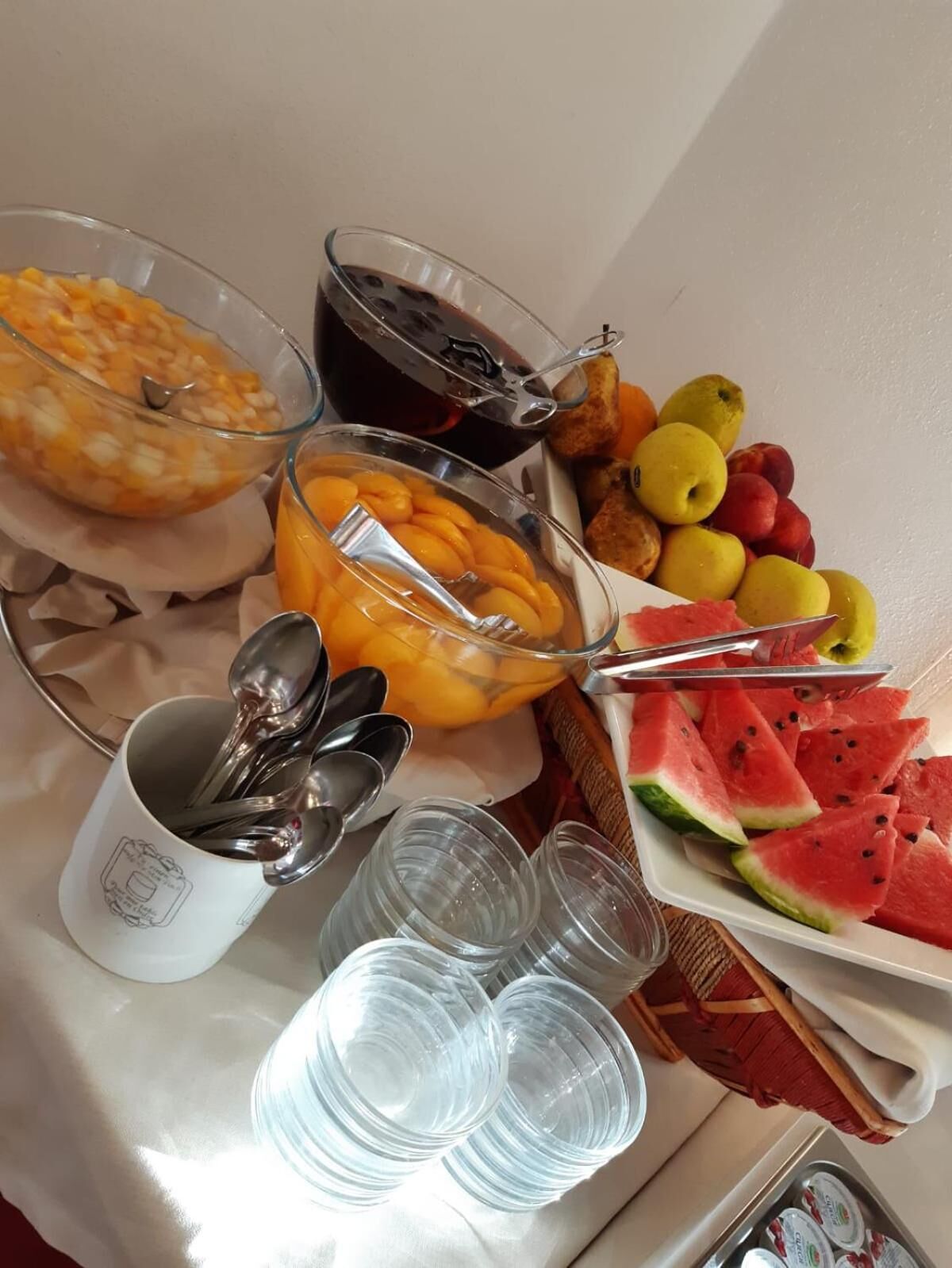 Ein Frühstücksbuffet mit verschiedenen Früchten, einer Orangenschale, einer Behälter mit dunkler Flüssigkeit und mehreren leeren Tassen.