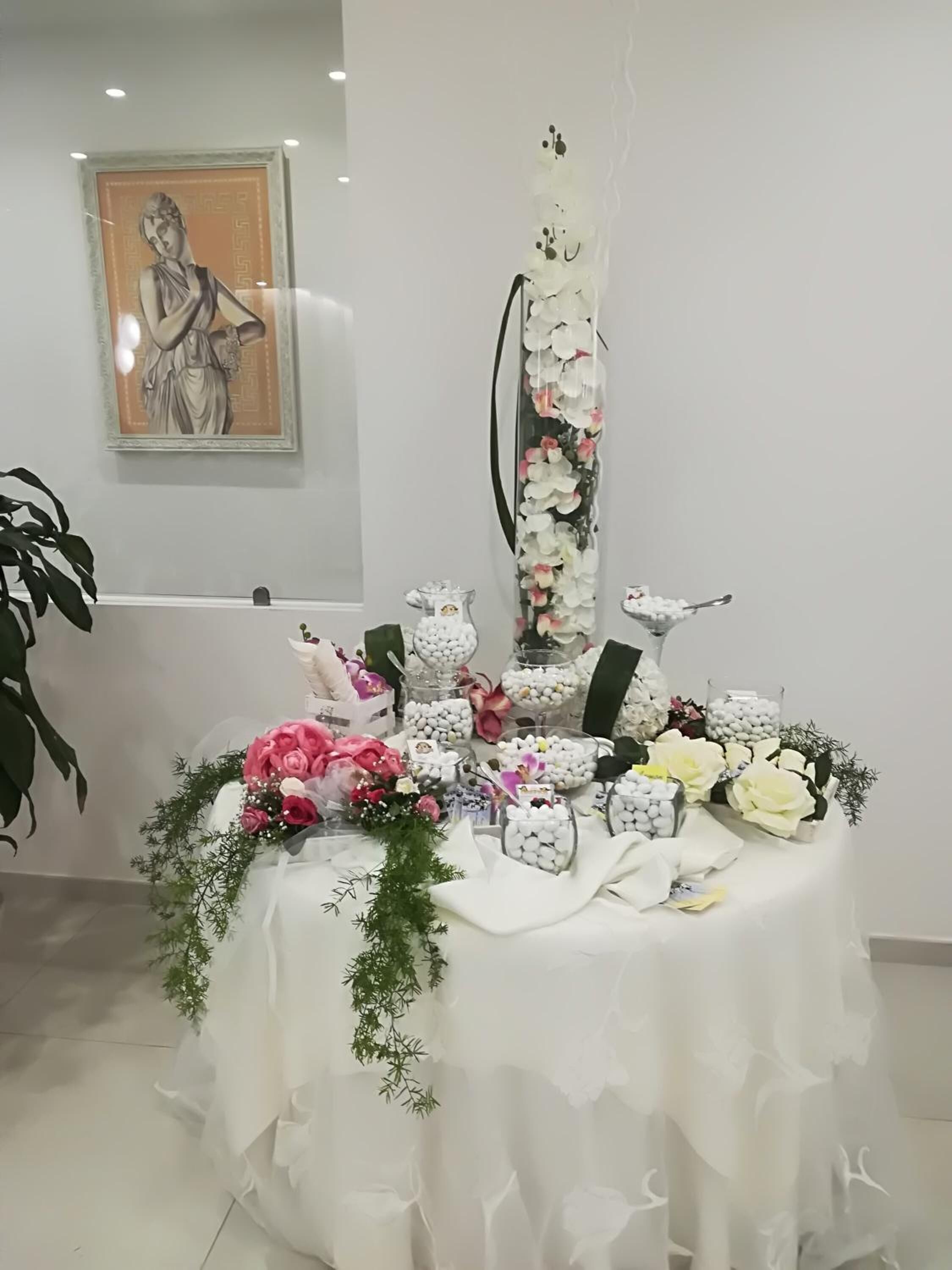 Une table recouverte d’une nappe blanche, agrémentée de fleurs, de roses blanches et roses, et surmontée d’un grand vase contenant des fleurs blanches.