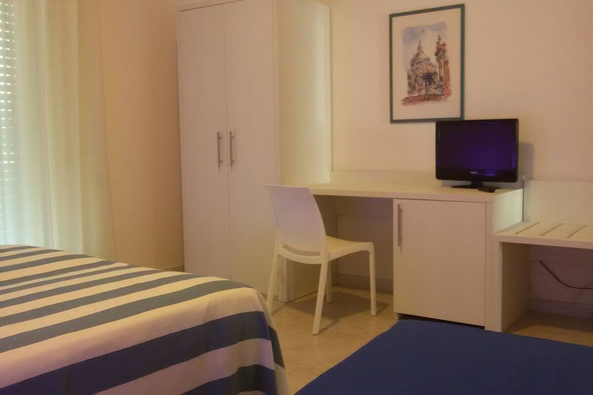 Ein Schlafzimmer mit einem Bett, einem Schreibtisch mit Stuhl, einem Fernseher und einem Kleiderschrank.