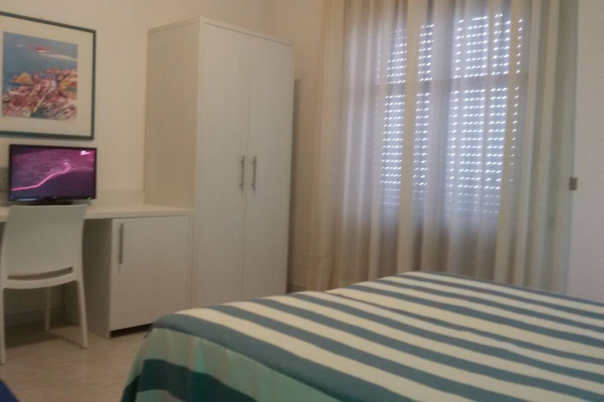 Ein Schlafzimmer mit Bett, Schreibtisch, Computer, Stuhl und Kleiderschrank.